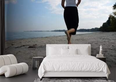 Bare feet of adult woman jogging on sand at the beach with seascape at background. Female legs running along sea shore. Happy lady spending time near ocean coast. Concept of summer vacation Wall mural