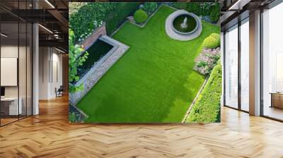 Overhead shot of a suburban backyard garden featuring an artificial grass lawn, a small pond with a fountain, and bordered by low hedges and flowering plants, ideal for relaxation and entertainment. Wall mural