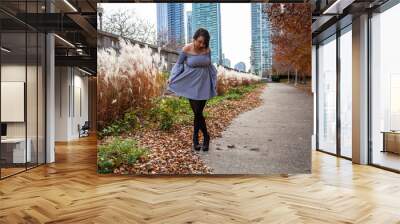 young beautiful fashion Latina woman wearing a trendy blue skirt is enjoying the outdoor park in the Chicago downtown metropolitan area. autumn is here as the color of the trees have change red  Wall mural