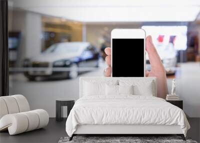 man hand using mobile smart phone with blank screen in a blurred background of car showroom Wall mural