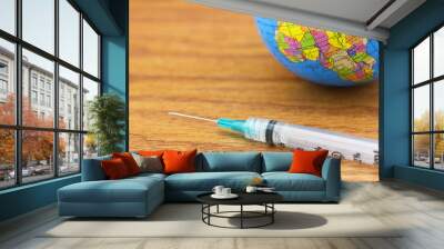 Global vaccine and worldwide medical equity symbolized in syringe and globe on wood grain background Wall mural