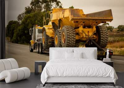 A very large haul dump truck being hauled by an 18 wheel truck down a freeway Wall mural