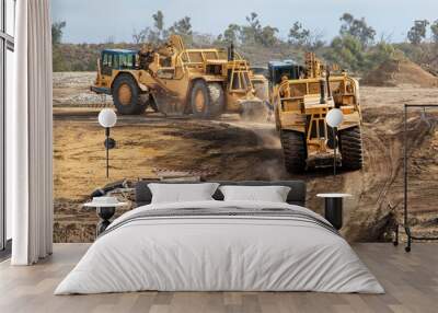 Heavy earthmoving equipment including scapers and motor graders involved in grading operations at a construction site Wall mural