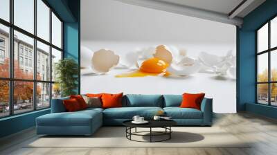 Cracked egg with yolk spilling out surrounded by empty eggshells, symbolizing food safety recall on clean white surface Wall mural