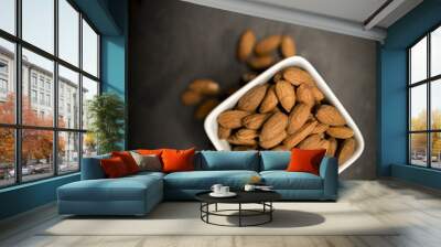 A white bowl of healthy and nutritious almonds shot from above on a black slate background Wall mural