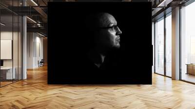 Side profile of a white middle aged man with spectacles or glass in shadow against a black background looking up towards the light Wall mural