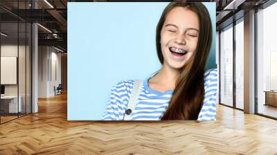 Cheerful beautiful young woman with dark hair and braces on teeth laughing isolated on a blue background. Wall mural