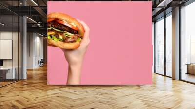 Close up portrait of a hungry young woman eating burger isolated over pink background Wall mural