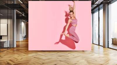 Happy athletic woman jumping in silhouette. Photo of sporty woman in fashionable pink sportswear on pink Wall mural