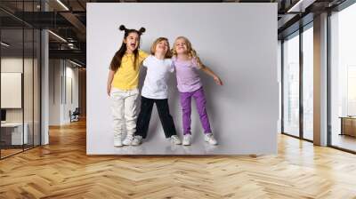 Little boy and girls dressed in colorful casual clothes. They are smiling and hugging each other, posing isolated on white Wall mural