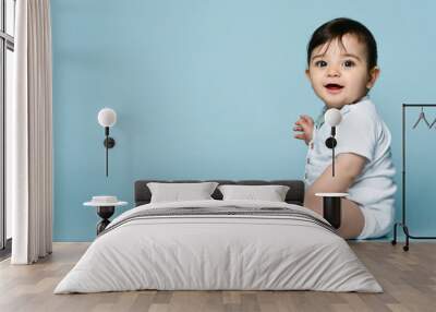 Little kid in white bodysuit as vest with bow-tie, barefoot. He smiling, sitting on the floor against blue background. Close up Wall mural