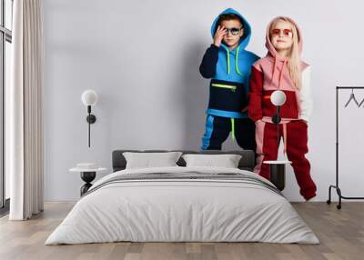 Little kids, boy and girl, in sunglasses and hoods, colorful tracksuits, sneakers. They posing isolated on white studio background Wall mural