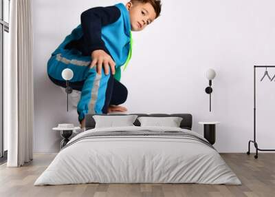 Little son in colorful tracksuit, sneakers. He performing exercises or kick by his leg, posing isolated on white background Wall mural