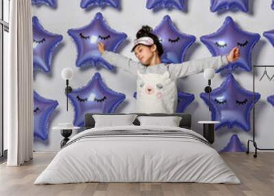 Portrait of a sleeping girl in home clothes, happily relaxing together at home and yawning because of insomnia, against the background of balloons in the shape of stars, purple-metallic color Wall mural