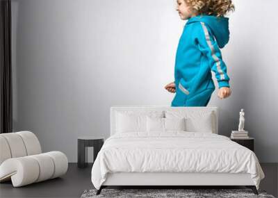 Running Active girl in a warm fashionable overalls, fashionable comfortable sportswear and sneakers walks in the studio. Child beauty model with blond curly hair advertising sportswear Wall mural