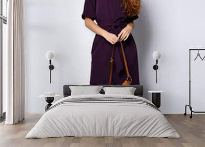 slender curly female model in a purple dark long dress and a small brown handbag, in full growth. Wall mural