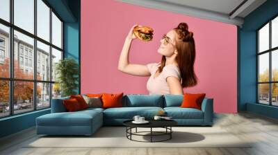 Woman eat burger sandwich with hungry mouth on pink background. Wall mural