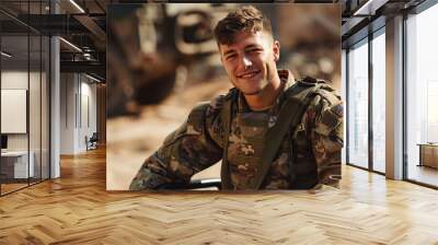 A disabled young male soldier wearing a happy camouflage uniform sits smiling looking at the camera in a wheelchair. Wall mural