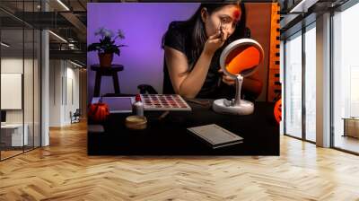 teenage girl putting on makeup for halloween with artificial makeup and wounds Wall mural