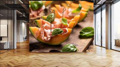 Sliced melon with ham and basil leaves, served on a wood chopping board Wall mural