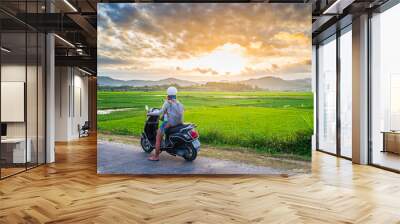 One person on motorbike looking at view of rice fields and mountains in the Phu Yen province, Nha Trang Quy Nhon, adventure traveling in Vietnam. Rear view sunburst backlight dramatic sky at sunset. Wall mural