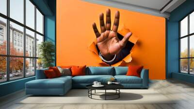 Open male hand breaks through an orange wall. Concept of breaking, changing, shock, marketing message Wall mural