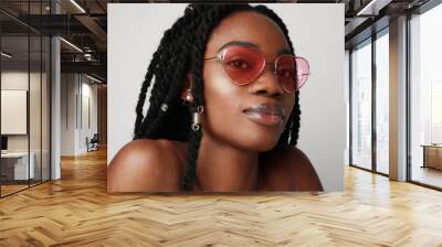 Young black woman with braids wearing pink sunglasses, posing on white wall. Wall mural