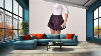 full length portrait of a brunette girl wearing a white shirt and plaid skirt uniform, standing pose in side profile against a cream studio background. Wall mural