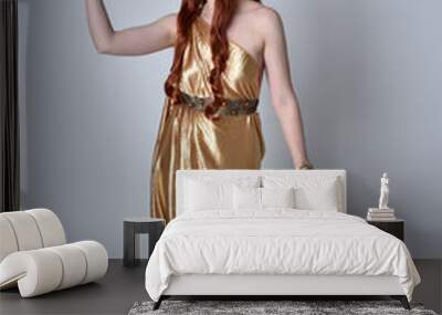 Full length portrait of girl with red hair wearing long grecian toga and golden wreath. Standing pose iisolated against a grey studio background. Wall mural