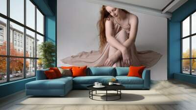 Full length portrait of pretty red haired woman dancer,  wearing skin toned flowing fairy dress. Sitting gestural poses  isolated on studio background. Wall mural