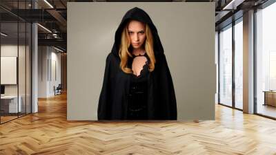 portrait of blonde woman wearing black hood, halloween witch costume.  creamy studio background. Wall mural