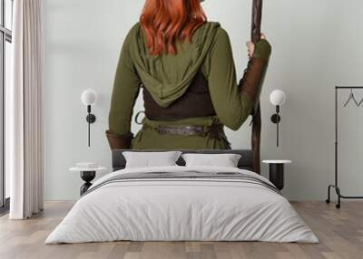 portrait of red haired female model, wearing green medieval fantasy costume with leather armour. Standing  pose facing away backwards with wood wizard staff weapon, isolated on white studio background Wall mural