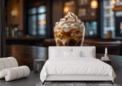 A glass of iced coffee with swirls of milk, topped with a generous amount of whipped cream and a drizzle of caramel sauce. The background is a cozy café setting Wall mural