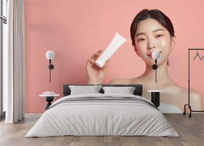 Beautiful perfect skin Korean woman holding a tube of face cream for a commercial on light pastel background, cosmetic mock up Wall mural