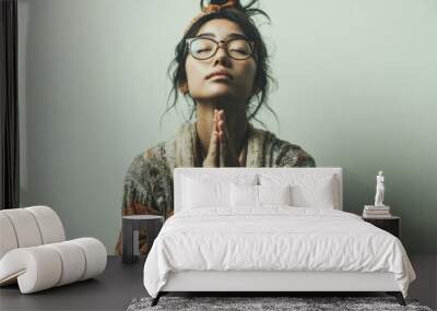 Woman in glasses and scarf praying on grey background. Wall mural