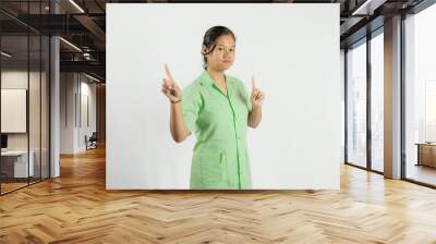 a young Asian nurse pointing her two fingers up with a happy expression and wears a green shirt, isolated on a white background
 Wall mural