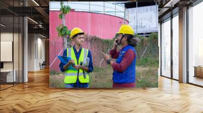 two Asian construction workers report by voice call while on a construction site, construction work concept. Wall mural