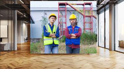 two Asian construction workers stand with their arms crossed at a construction site, construction work concept. Wall mural