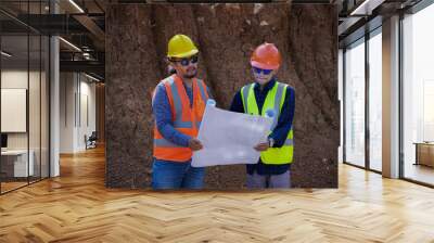 Two young male construction workers are surveying using blueprints in the field Wall mural