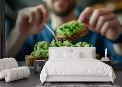 A soft focus image shows a man enjoying a hearty and delectable breakfast in a hip café or restaurant. He is ready to indulge and satisfy his hunger by spreading avocado spread or guacamole over rye b Wall mural