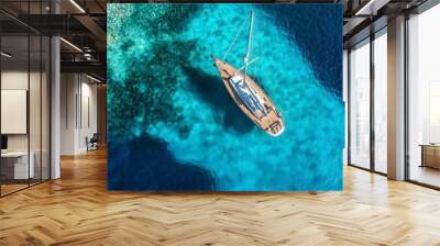 An ultra-wide aerial drone photo shows a sailboat anchored in calm, tropical, turquoise waters, creating a blue lagoon. Wall mural