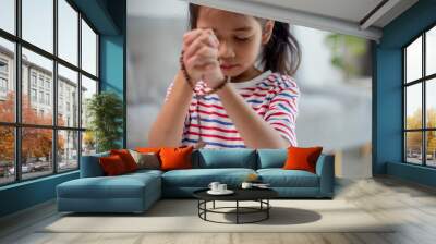 Christian concept. Little Asian girl praying withholding the cross. Concepts of hope, faith, Christianity, religion, Wall mural