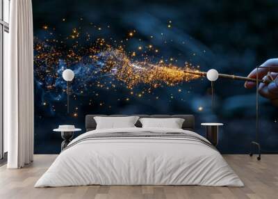 A hand holding a magic wand casting sparkling golden particles against a dark wooded background Wall mural