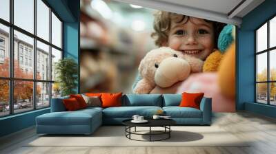 A smiling young child with light curly hair hugs a large plush toy while standing in a colorful toy store aisle, showcasing a sense of joy and happiness in the moment. Wall mural