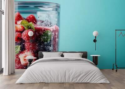 A vibrant and refreshing image showing a clear glass filled with a mix of fresh and colorful fruits, such as raspberries and blueberries, garnished with mint leaves on a teal background. Wall mural