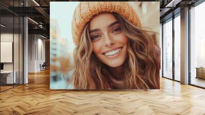 A woman with flowing hair beams at the camera in a winter street, wearing a cozy knit hat. The image captures the essence of joy and simple elegance. Wall mural