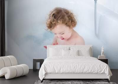 Little baby girl with curly hair playing with foam in a bath Wall mural