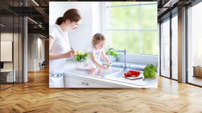 Young mother and her adorable toddler daughter cooking salad Wall mural