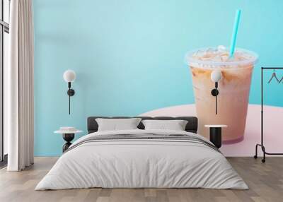 Iced coffee in a clear plastic cup with a blue straw on a pink platform against a blue background. Wall mural