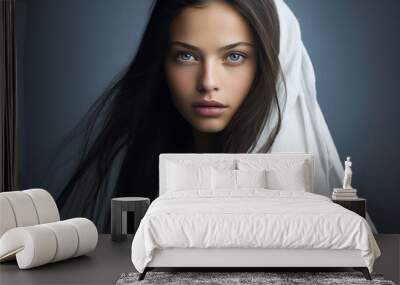 Close-up portrait of a very beautiful young woman with green eyes, and long dark brown hair, wearing a white top and a white veil or head covering - copy space, isolated, blue background Wall mural